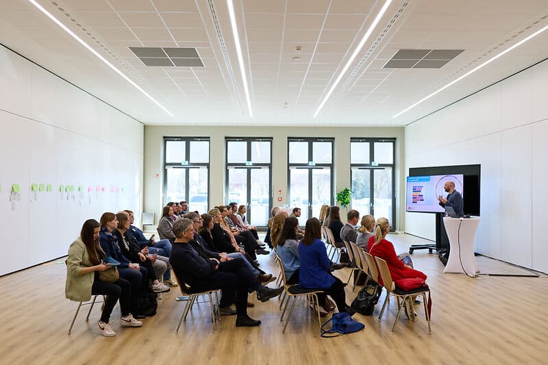 Beteiligte eines Workshops schauen auf einen Bildschirm auf dem eine Präsentation zu sehen ist.