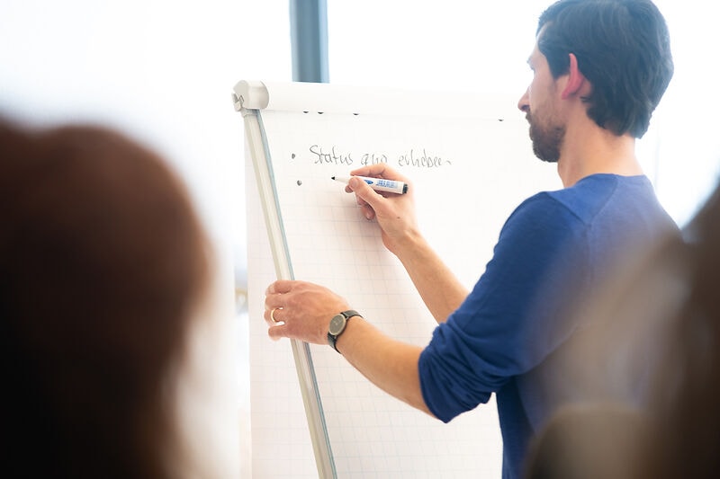 Person, die mit einem Stift auf einer Flipchart schreibt.